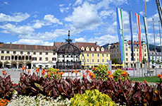 Der Brucker Hauptplatz - blühende Blumen im Vordergrund, dahinter der Eiserne Brunnen und die historischen Gebäude der Stadt