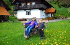 Junge und Mädchen sitzen vor dem Almgasthaus Hutterer auf einen Baumstumpf