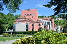 Außensicht von Brucker Stadtsaal: ein großes rosarotes Gebäude, umgeben von Grünflächen und Bäumen