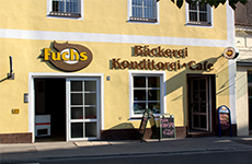 Die Fuchs J. Bäckerei, typisches, gelbes Haus mit Logo der Bäckerei