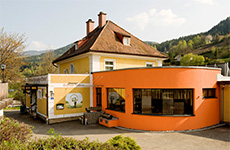 Der Gasthof "Zum lustigen Steirer" in Oberaich mit modernem, orangem Zubau und mitten in der Natur