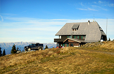 Das Schutzhaus am Rennfeld aus Holz, fast am Gipfel liegend, mit einem Auto daneben
