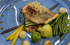 Ein Fischstück ist auf einem blauen Teller platziert, daneben befindet sich grünes Gemüse.