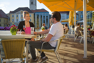 Das Sonnenoase Café direkt am Hauptplatz mit gelben Sonnenschirmen mit dem Uhrturm der Stadtpfarrkitche und dem Rathaus im Hintergrund