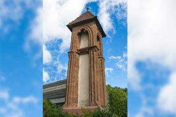 Ein steinerner quadratischer Turm mit Dach und einem christlichen Kreuz an der Spitze
