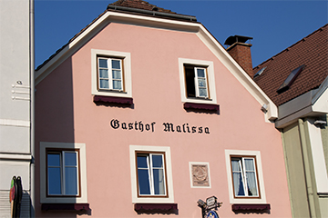 Der Gasthof Malissa, ein rosarotes Gebäude, darauf der Name des Gasthofs und blauer Himmel