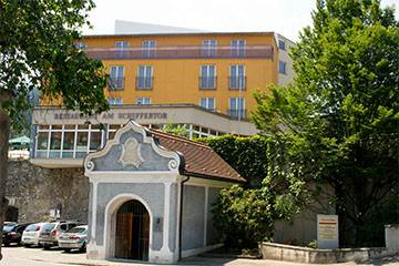 Das Hotel Landskron mit seinem Restaurant "Am Schiffertor", ein gelbliches, großes Gebäude mit dem Haupteingang und Mauer bzw. Wand aus Stein, und mit großer Parkgarage