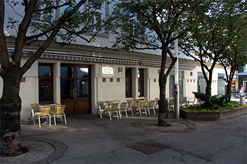 Das Lokal Life Style, in der Burggasse, weißes Gebäude mit Tischen und Sesseln im Freien und brauner Eingangstür, davor Bäume