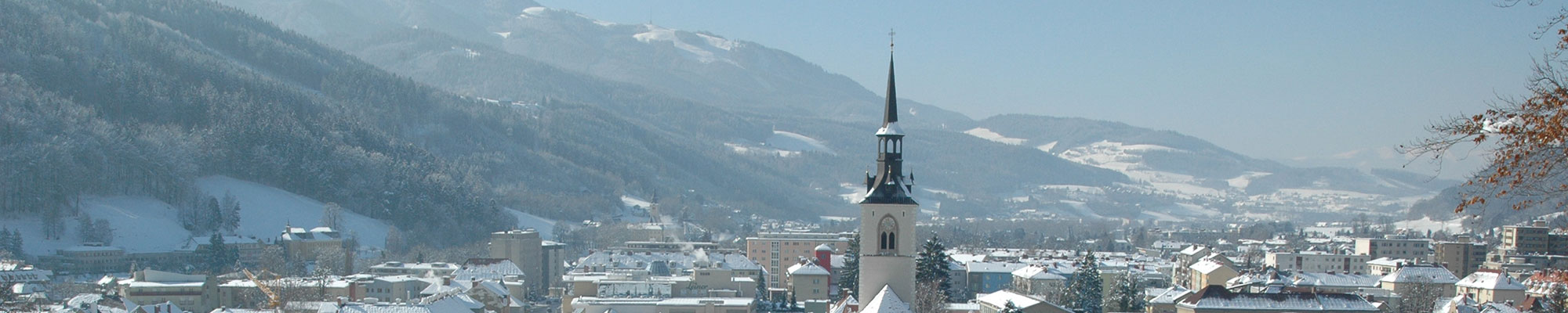 Blick vom Schlossberg auf die verschneite Stadt Bruck an der Mur - im Vordergrund die Pfarrkirche und dahinter das herrliche Bergpanorama