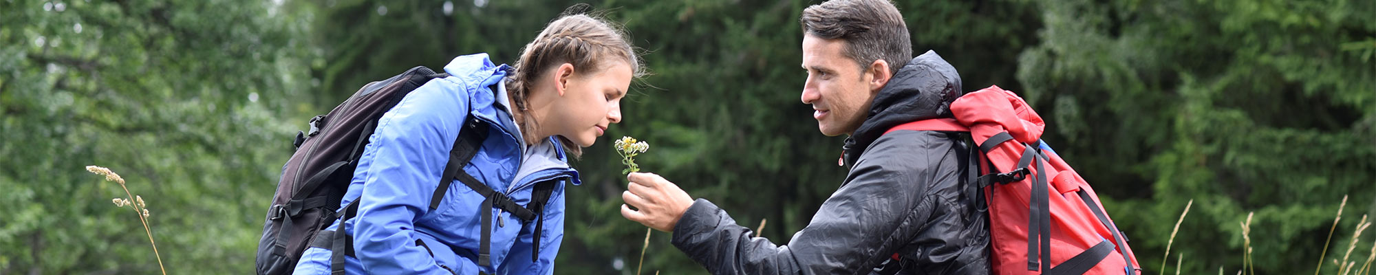 Wanderpärchen sitzt auf einen Baumstamm und die Frau riecht an einer Blume.