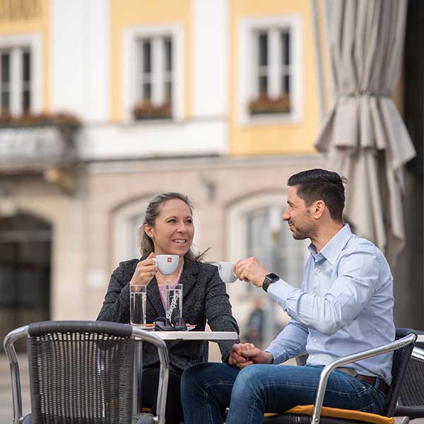 Ein Mann und eine Frau sitzen im Gastgarten und trinken einen Kaffee